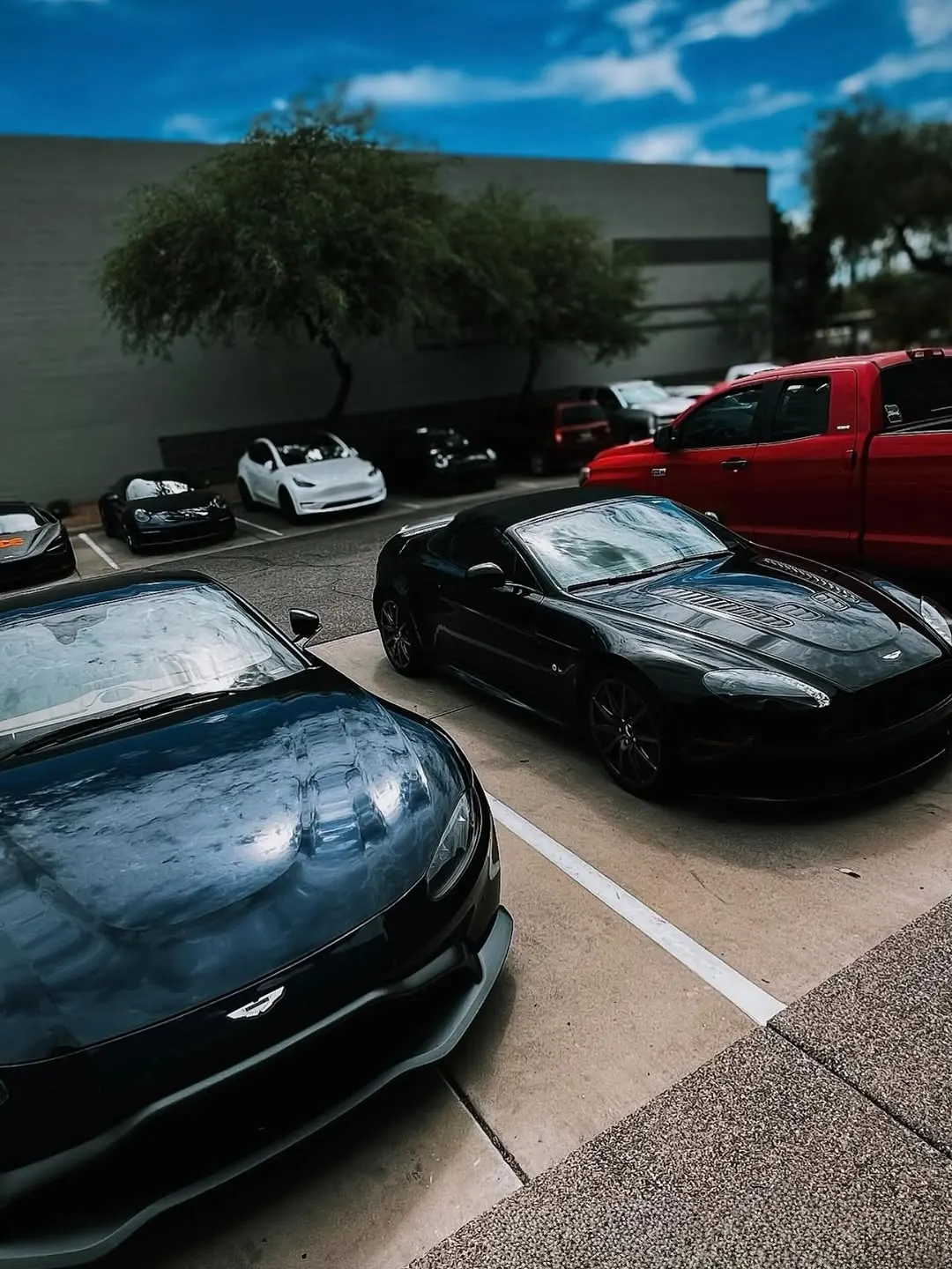 Two dark Aston Martin Vantages from different generations, parked outside the shop