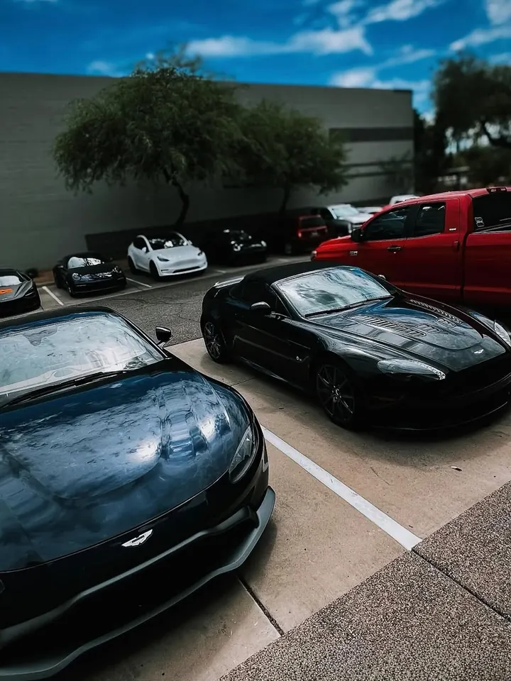 Two dark Aston Martin Vantages from different generations, parked outside the shop
