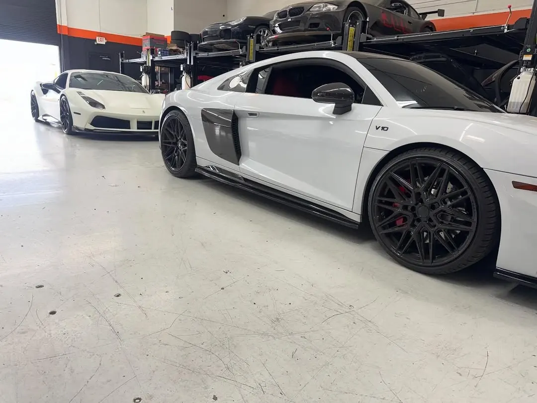 White Audi R8 V10 with black wheels in the shop, a white Ferrari 488 behind it