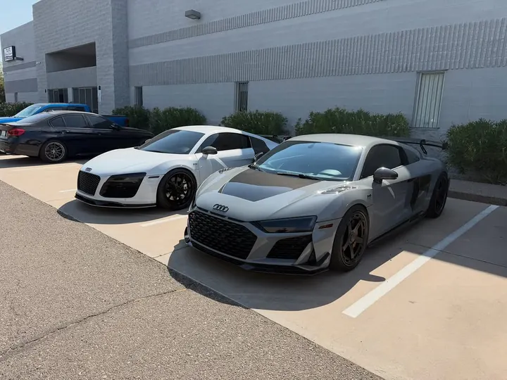 White first-generation and grey second-generation Audi R8 parked side by side outside the shop