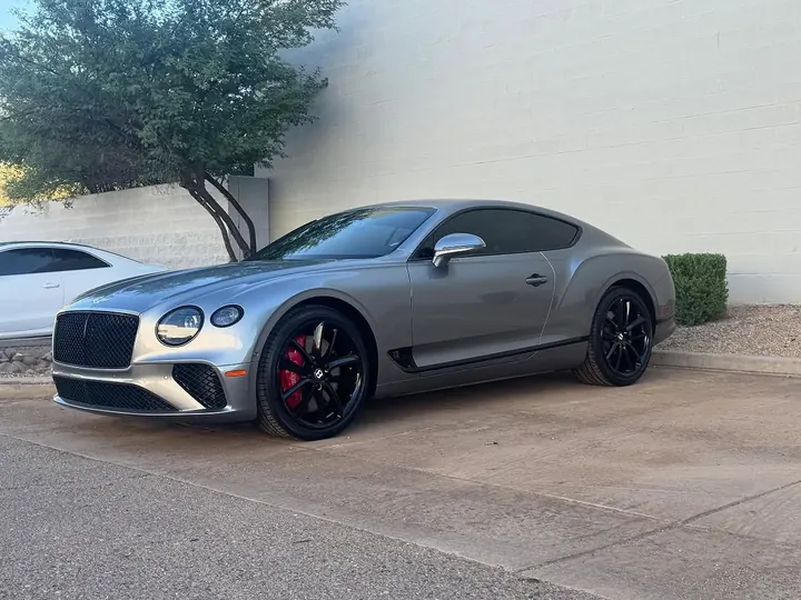 Silver Bentley Continental GT with black wheels and red brake calipers, parked outside the shop