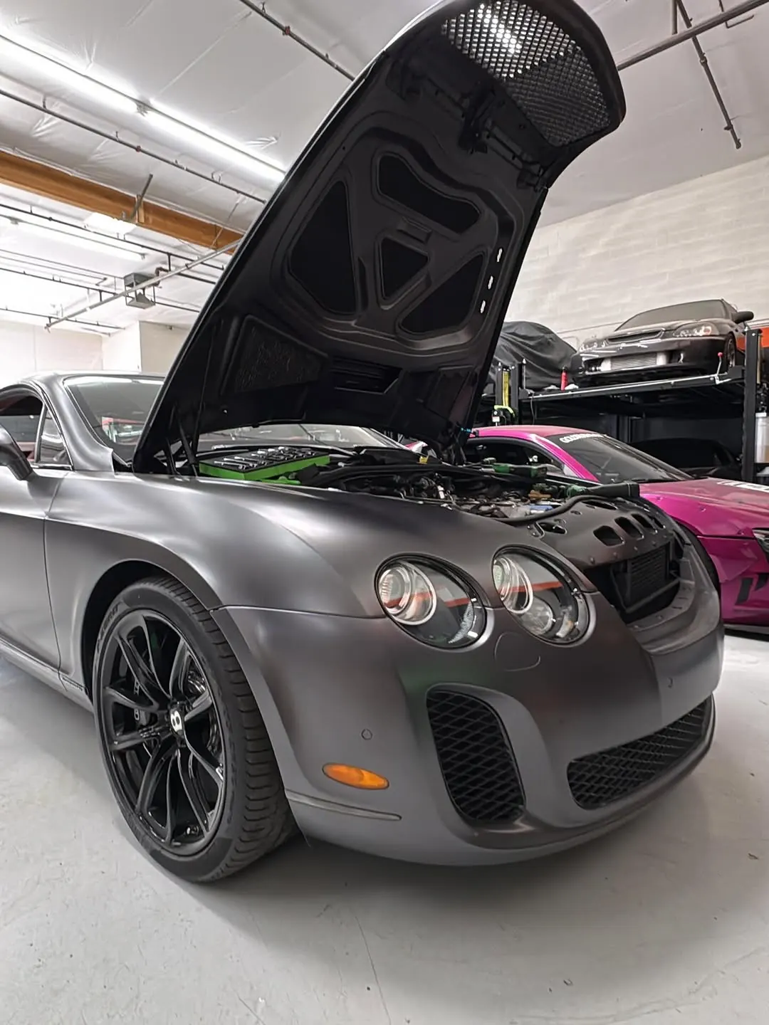 Matte grey Bentley Continental Supersports with its hood open in the shop