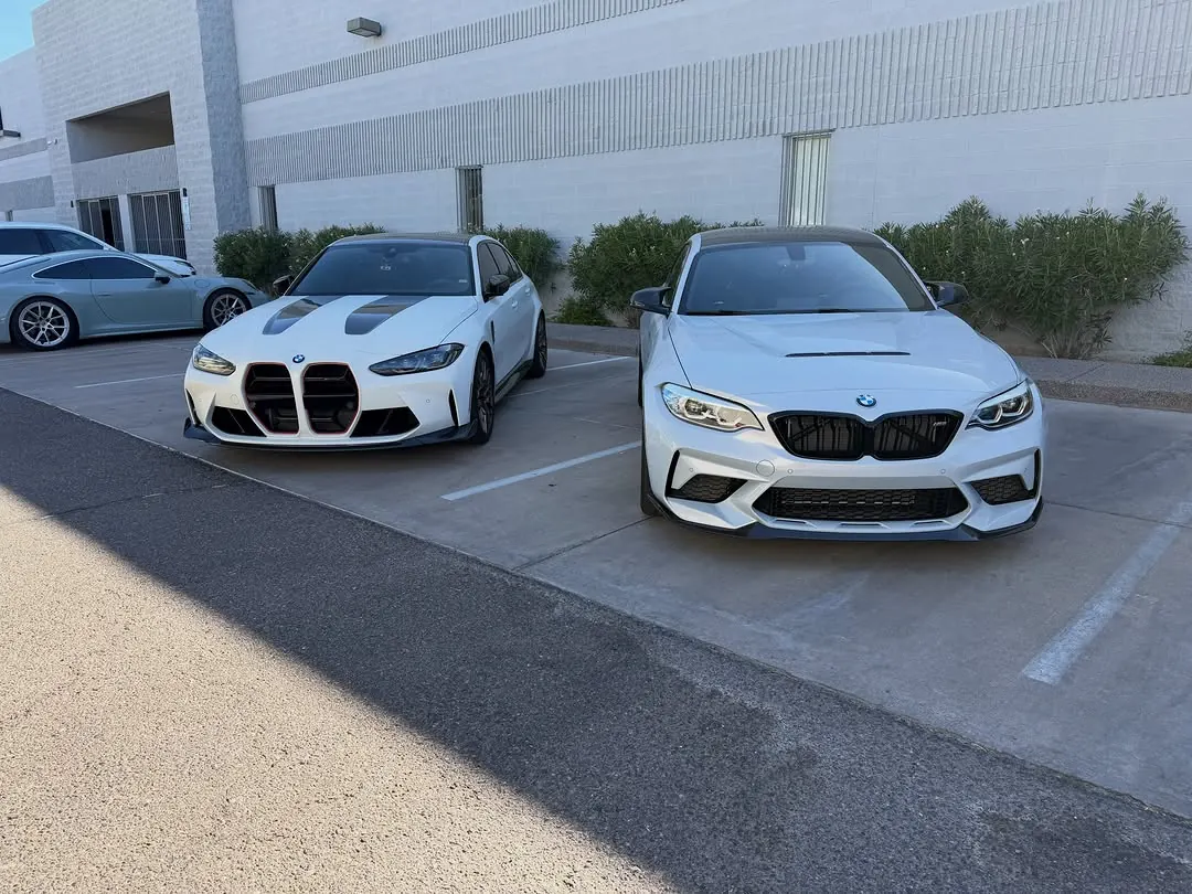 White BMW M3 CS (G80) and M2 CS (F87) parked side by side outside the shop