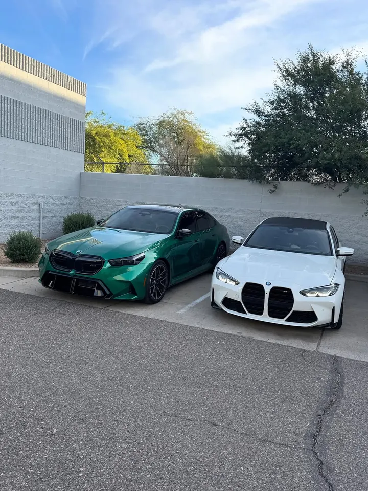 Green BMW M5 (G90) and white BMW M3 (G80) parked side by side outside the shop
