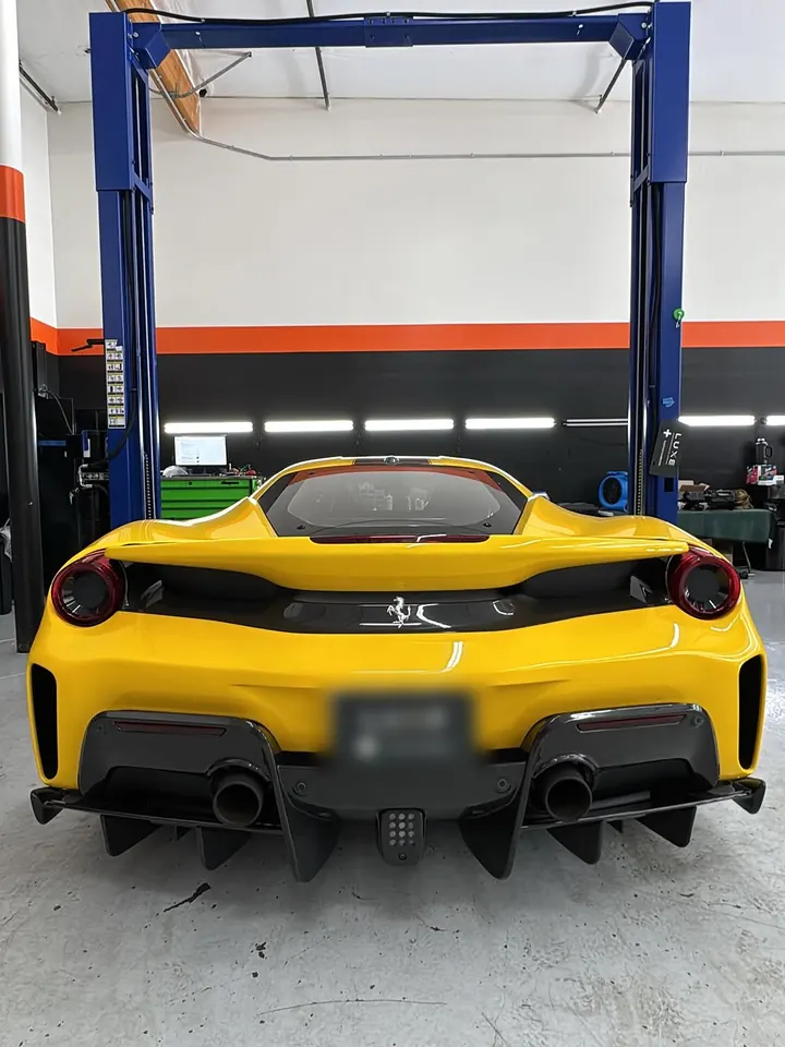 Yellow Ferrari 488 Pista seen from behind, parked under a lift in the shop