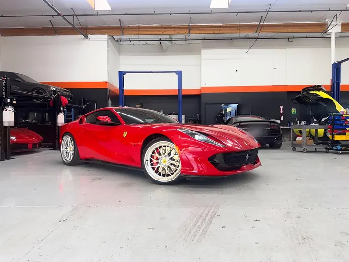 Red Ferrari 812 Superfast with polished multi-spoke wheels, parked in the shop
