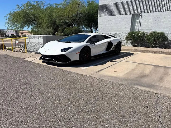 White Lamborghini Aventador Ultimae with black wheels, parked outside the shop