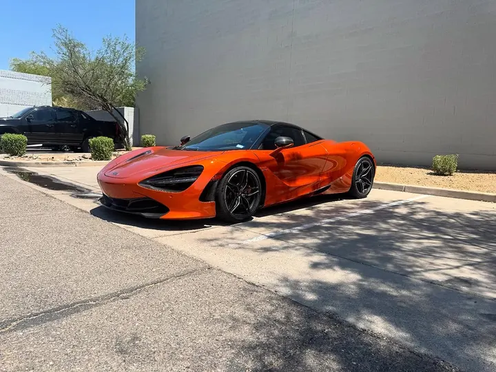 Front three-quarter view of an orange McLaren 720S parked outside the shop
