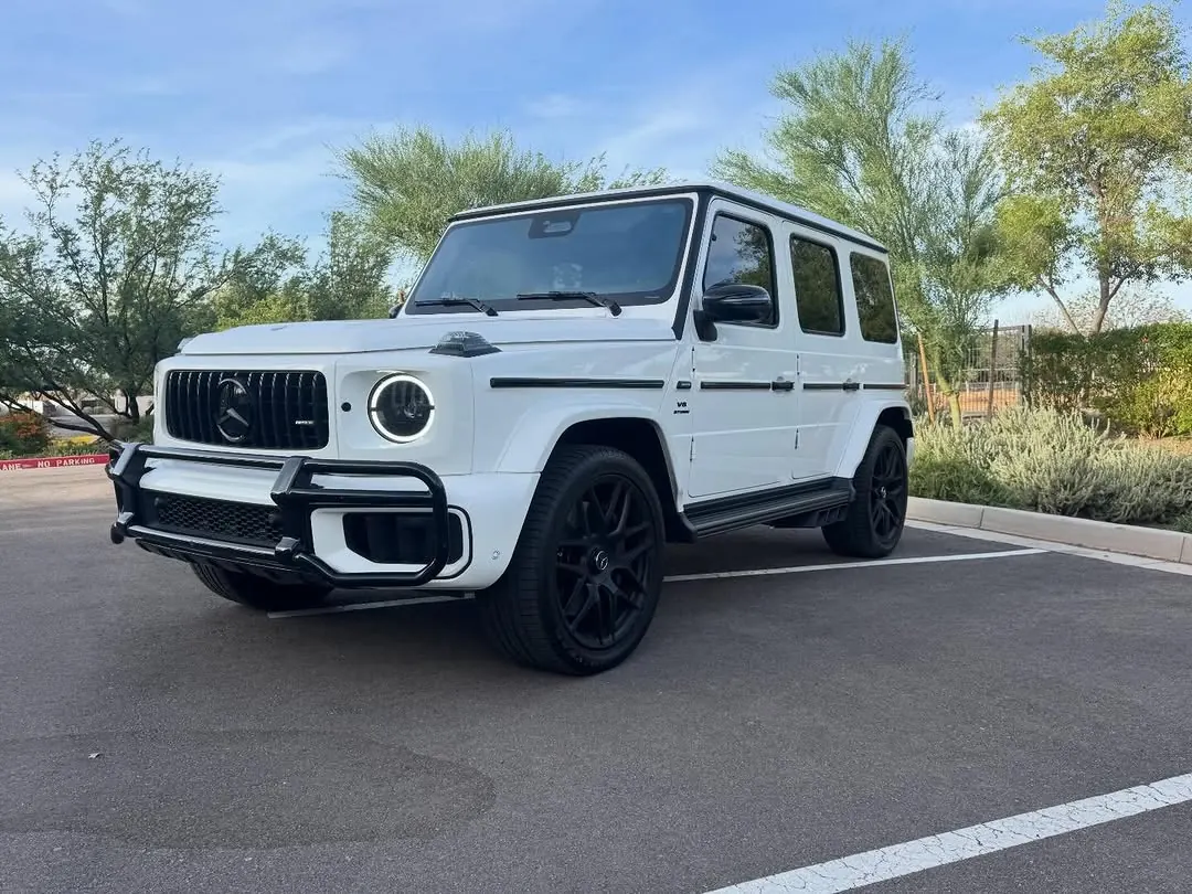 White Mercedes-AMG G63 with black wheels and a front grille guard in a parking lot