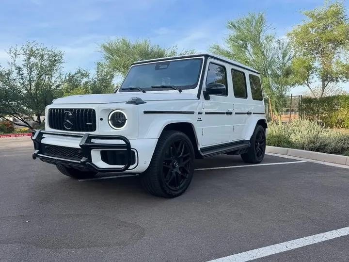 White Mercedes-AMG G63 with black wheels and a front grille guard in a parking lot