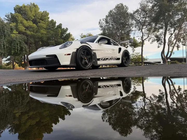 White Porsche 911 GT3 RS (992) with black wheels, reflected in a rain puddle