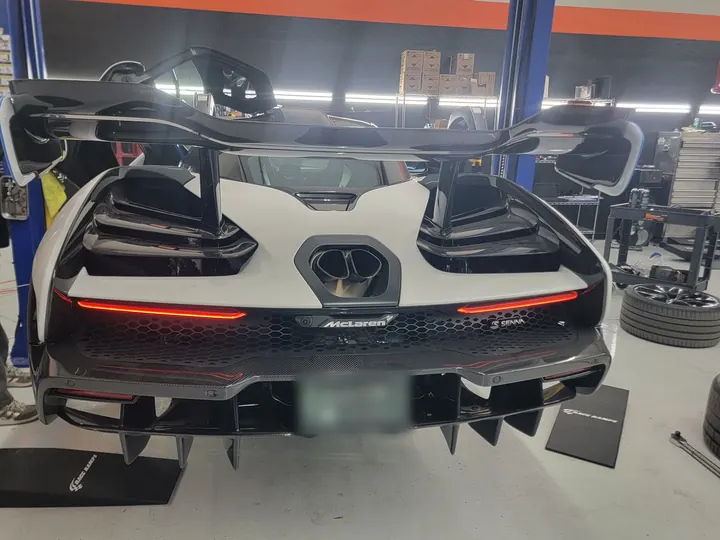 Rear of a white McLaren Senna in the shop, with one door raised
