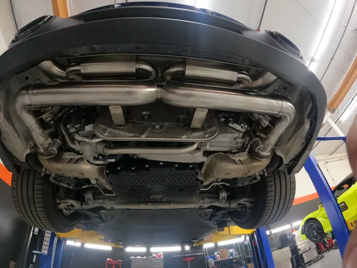 Underside of a dark blue Porsche 911 (992) on a lift, showing its new exhaust