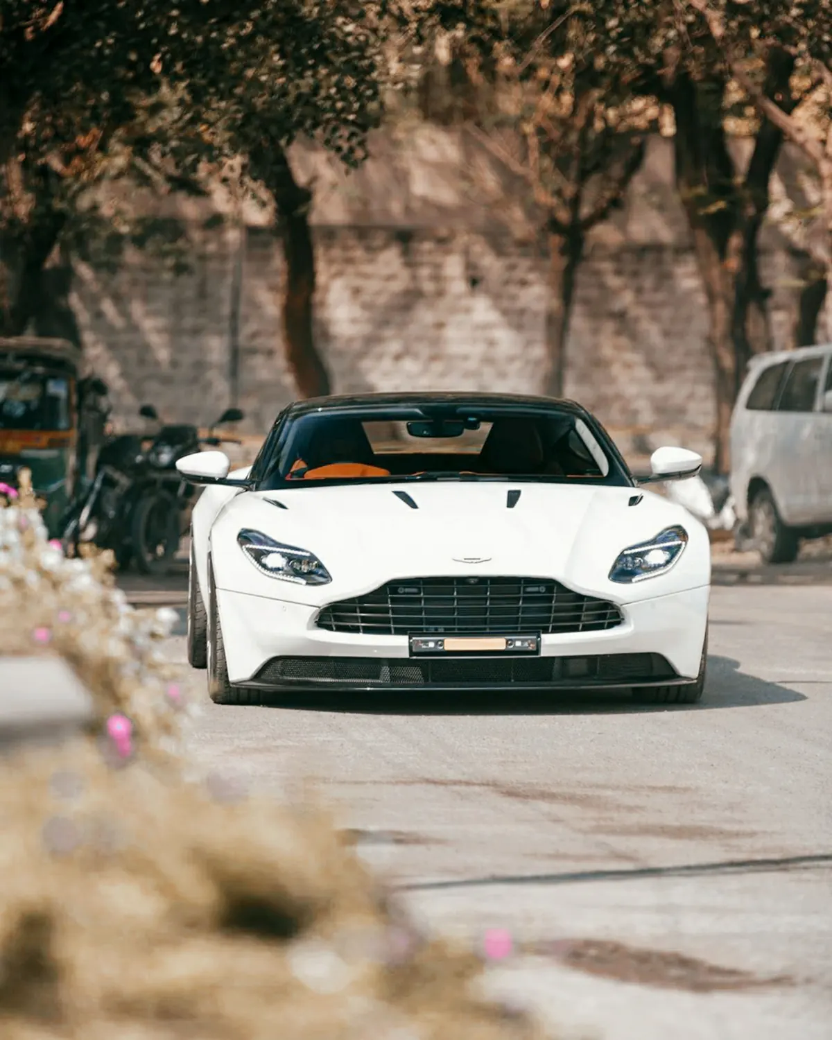 Front view of a white Aston Martin DB11 AMR with a black roof on a tree-lined street
