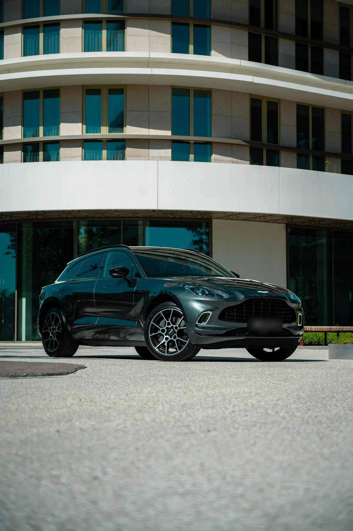 Front three-quarter view of a dark green Aston Martin DBX parked outside a curved modern building