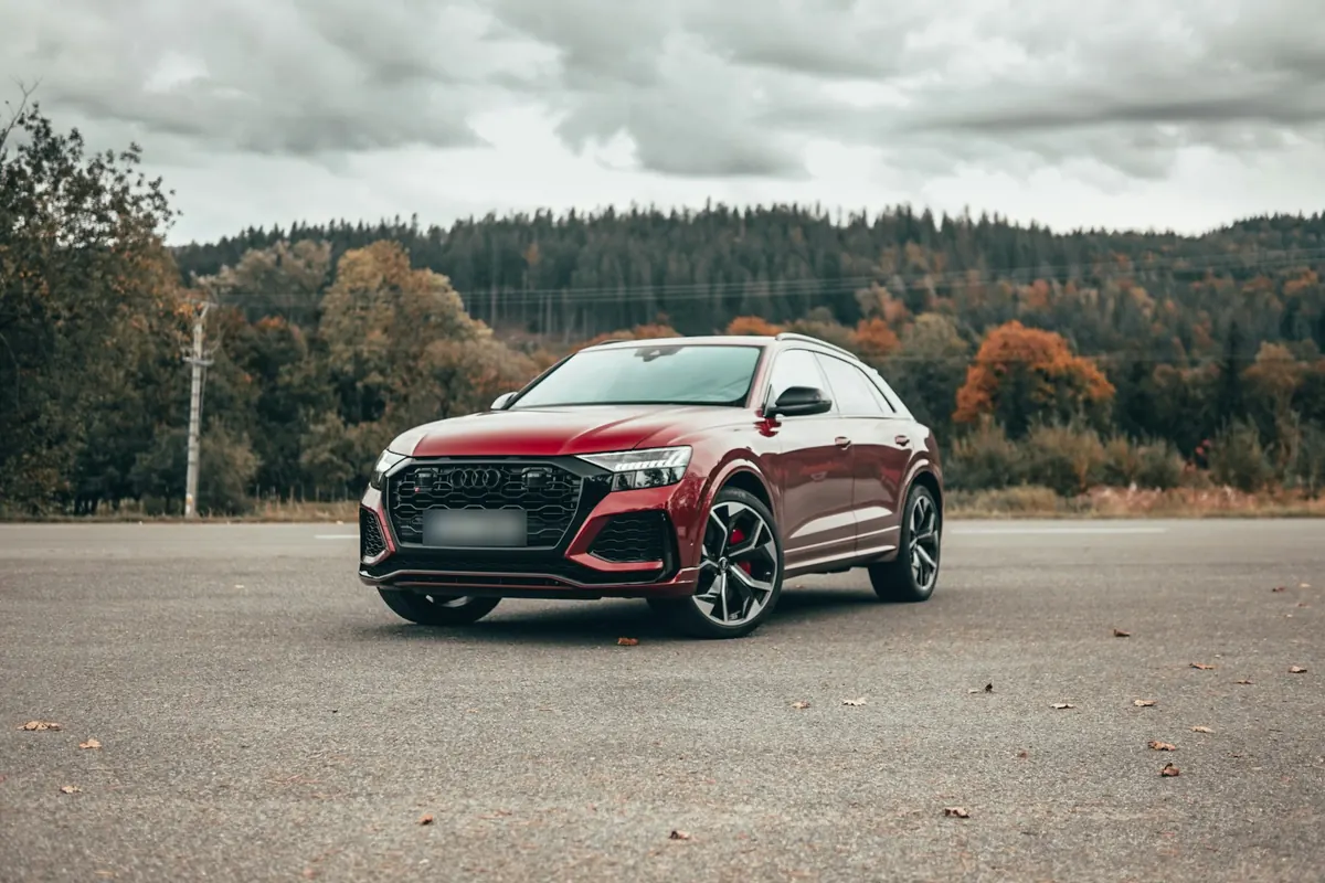 Front three-quarter view of a red Audi RS Q8 on an empty lot with autumn trees