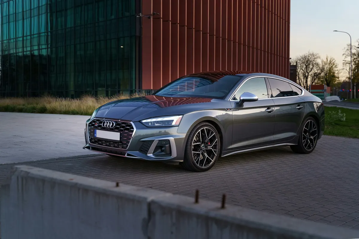 Front three-quarter view of a grey Audi S5 (B9) Sportback parked by a modern building