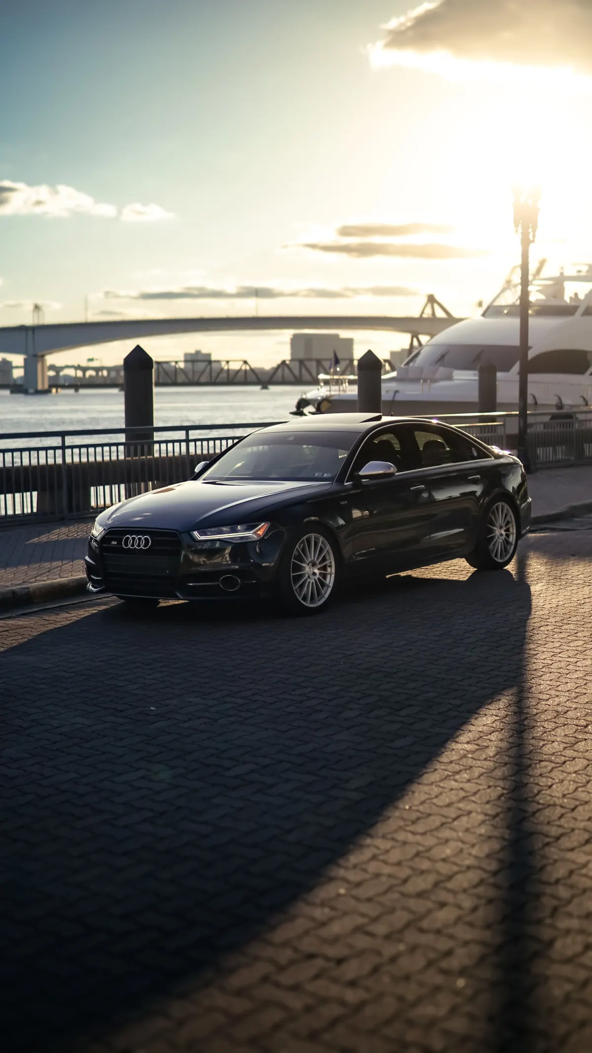 Front three-quarter view of a black Audi S6 (C7) sedan by a waterfront at sunset