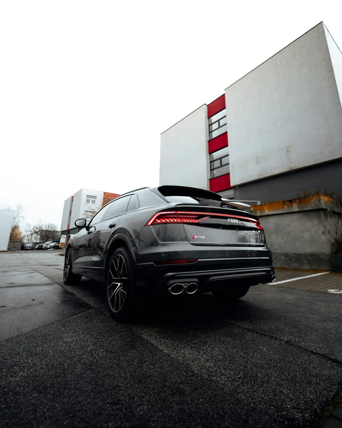 Rear three-quarter view of a grey Audi SQ8 parked by a white building