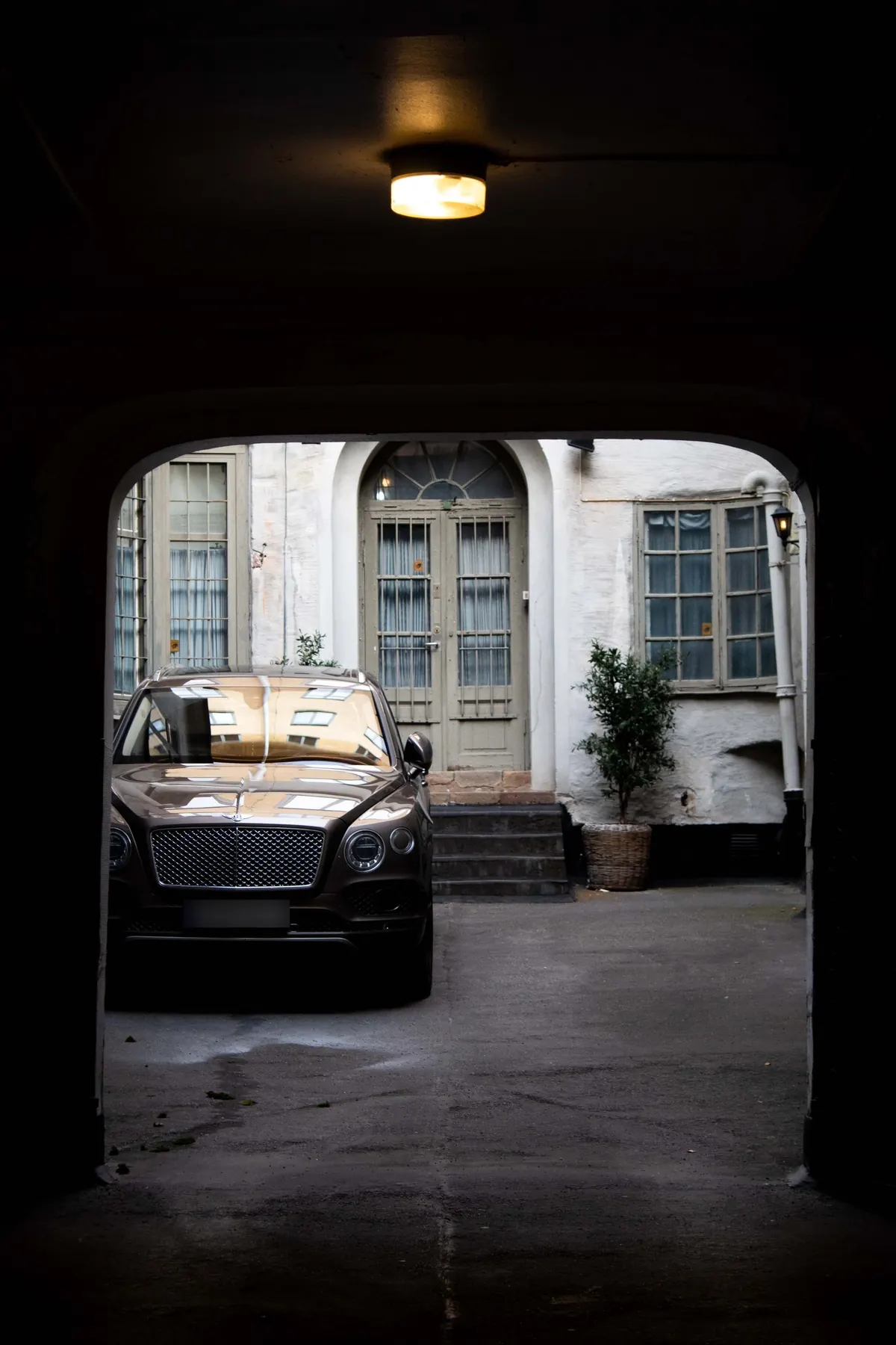 Front view of a brown Bentley Bentayga W12 in a courtyard, seen through an archway