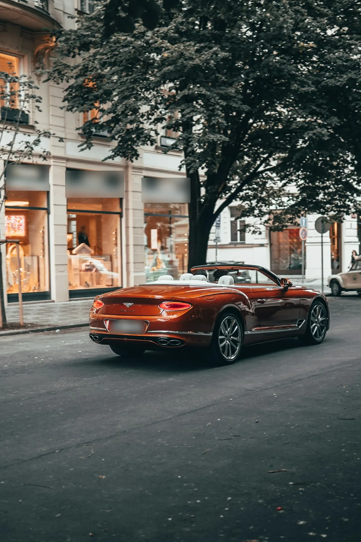Rear three-quarter view of a copper Bentley Continental GTC V8 (third generation) with the roof down on a city street