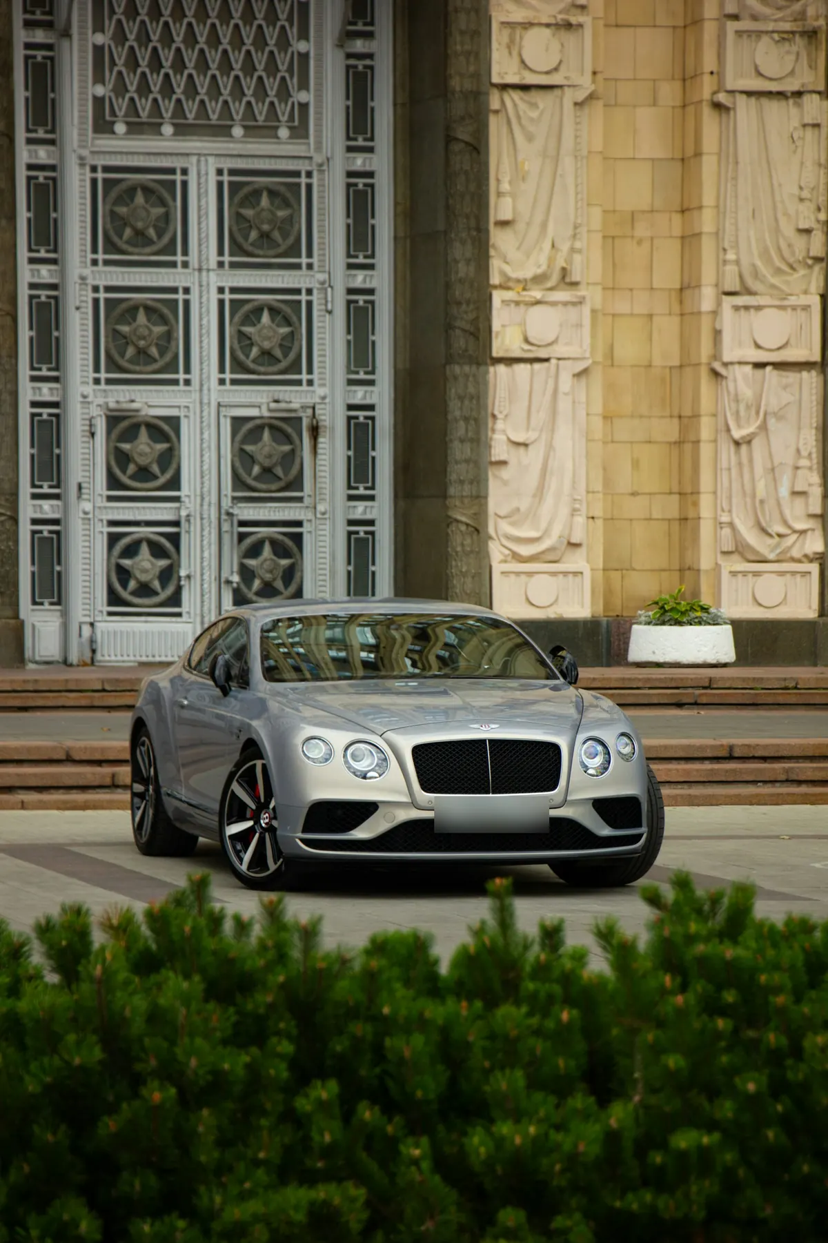 Front three-quarter view of a silver Bentley Continental GT V8 (second generation) outside a stone building