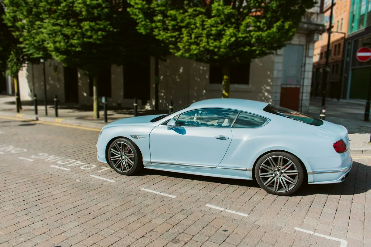 Side view of a light blue Bentley Continental GT3-R coupe parked on a brick street