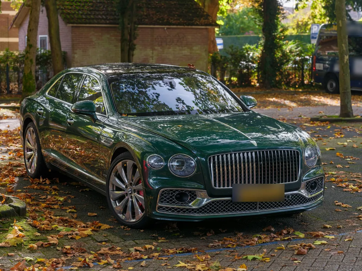 Front three-quarter view of a dark green Bentley Flying Spur W12 Mulliner parked among fallen leaves