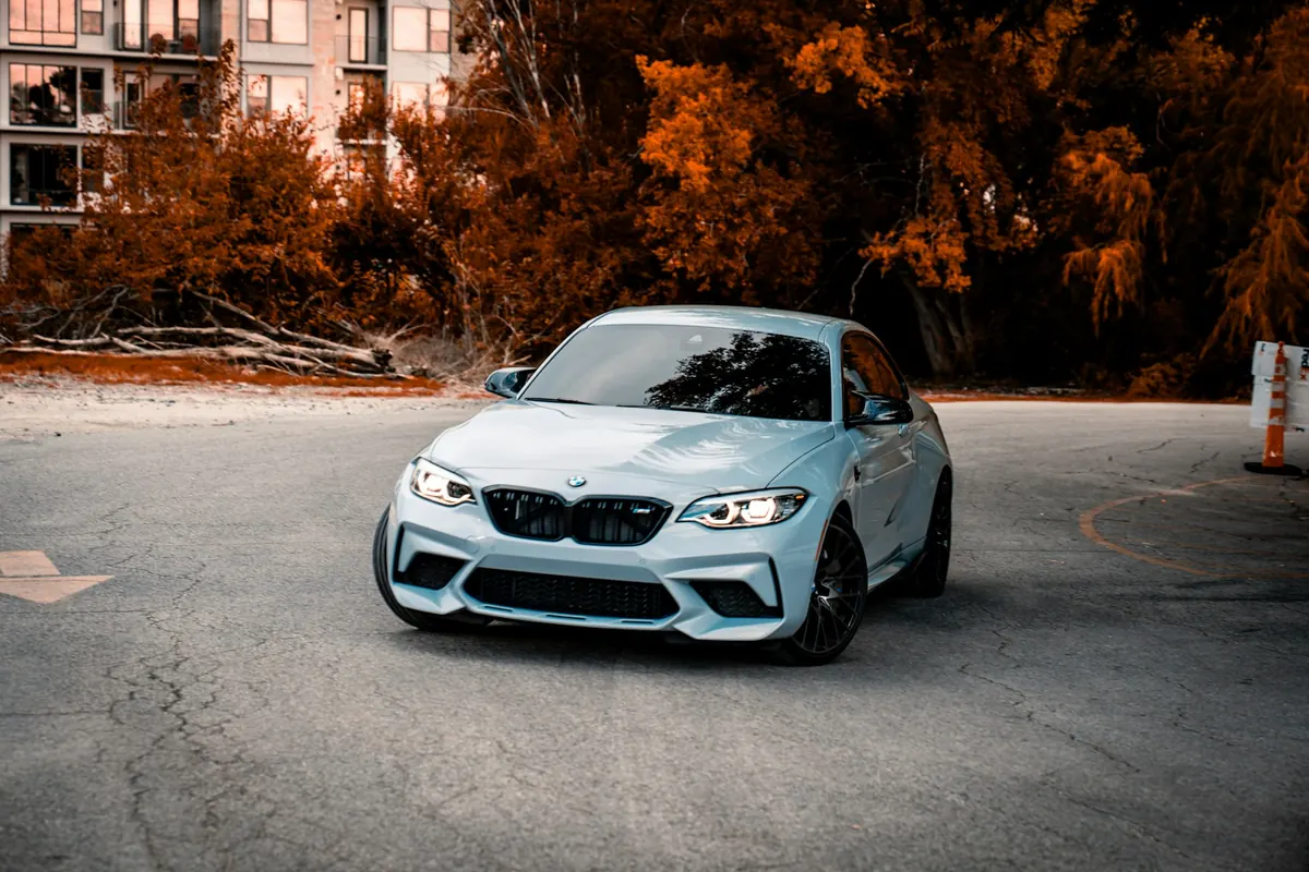 Front three-quarter view of a silver BMW M2 Competition (F87) on an empty road with autumn trees