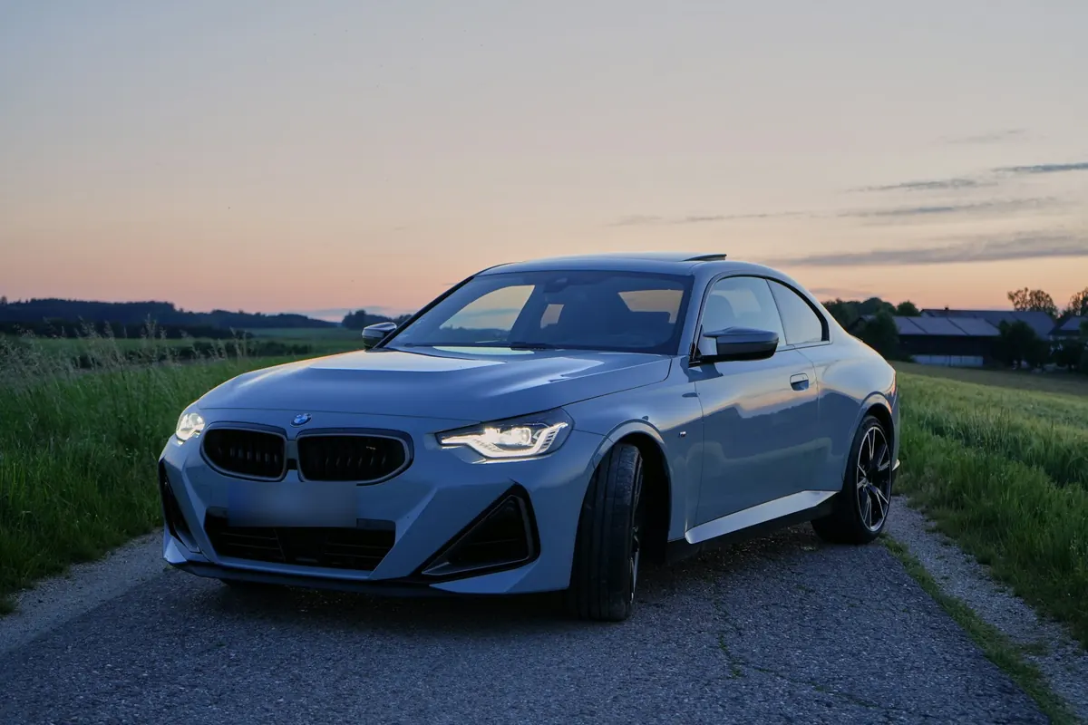 Front three-quarter view of a grey BMW M240i (G42) coupe on a country road at dusk