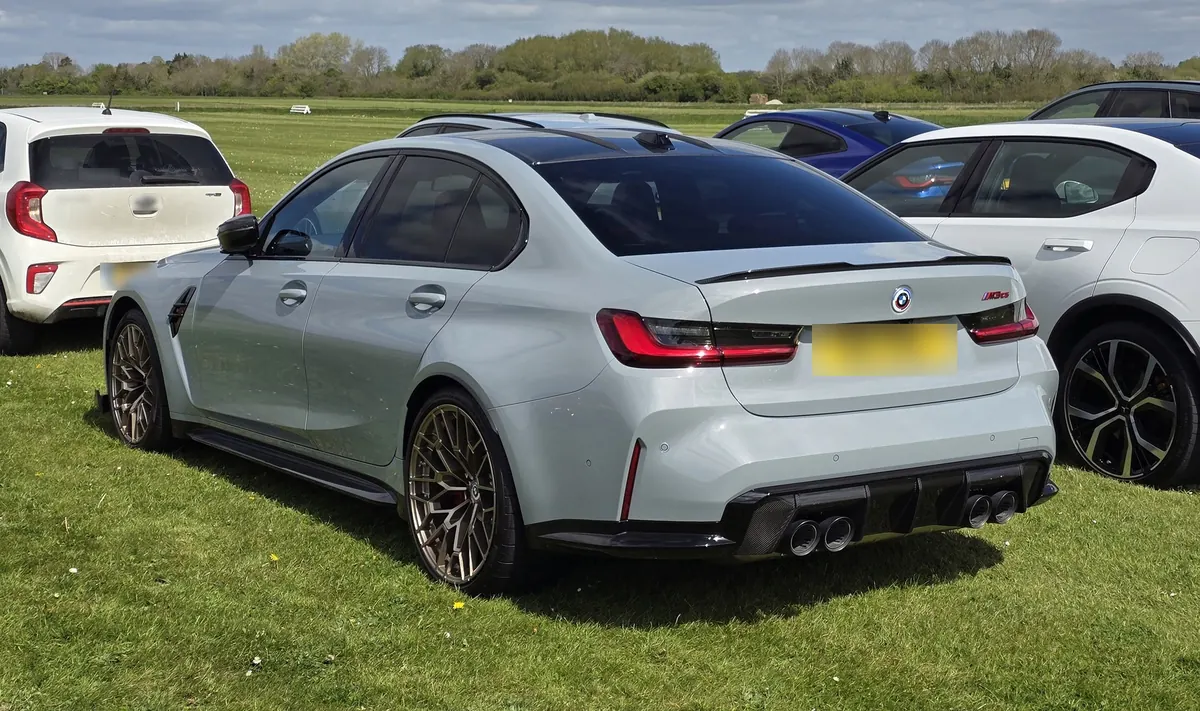 Rear three-quarter view of a grey BMW M3 CS (G80) parked on grass