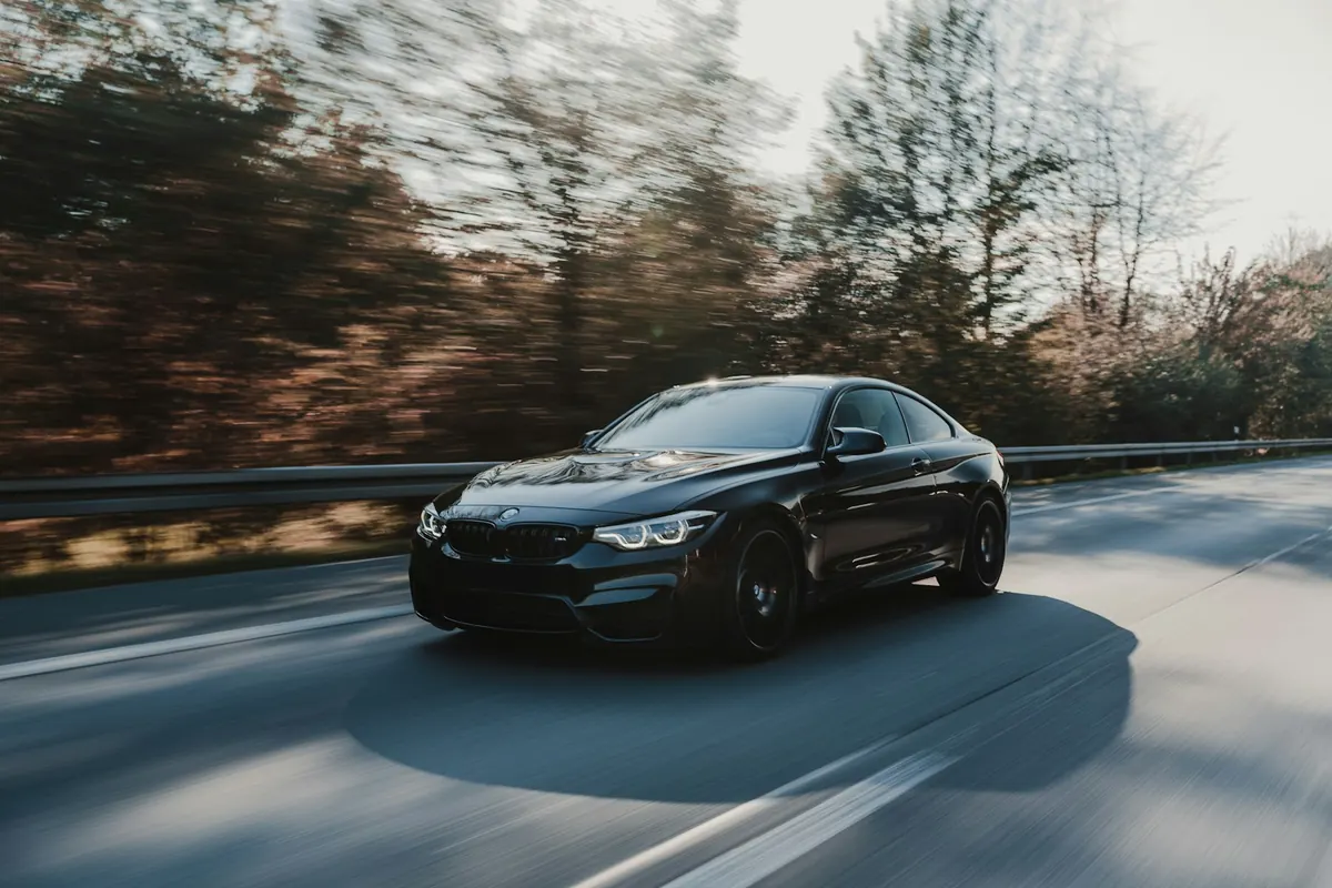 Front three-quarter view of a black BMW M4 (F82) coupe driving on a country road