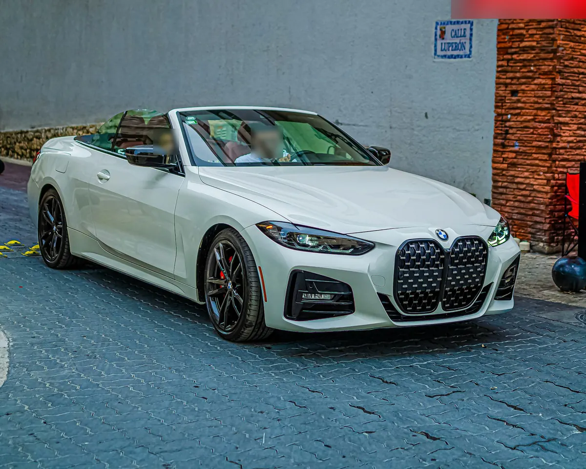 Front three-quarter view of a white BMW M440i Convertible (G23) with the roof down on a cobbled street