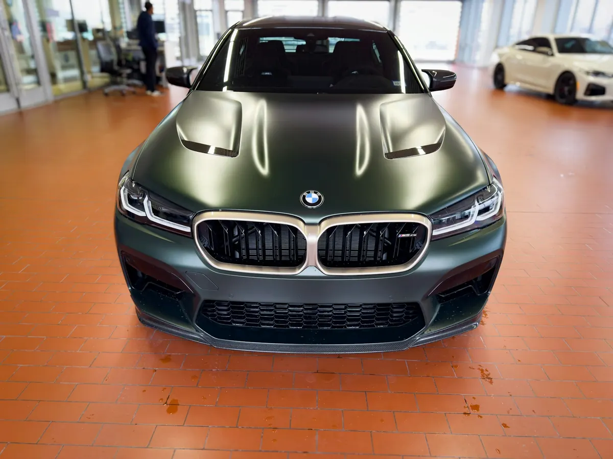 Front view of a matte green BMW M5 CS (F90) in a showroom