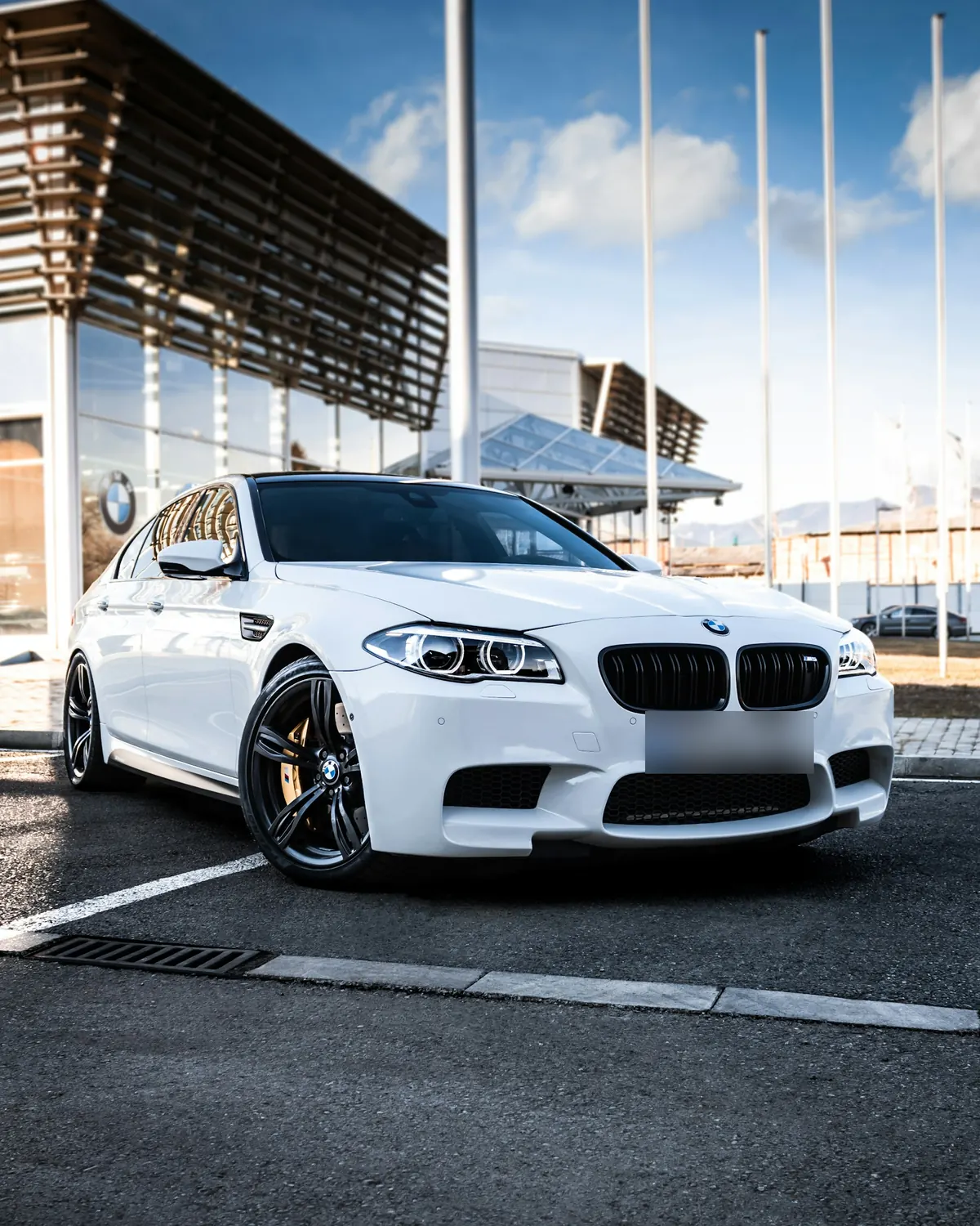 Front three-quarter view of a white BMW M5 (F10) sedan outside a BMW showroom