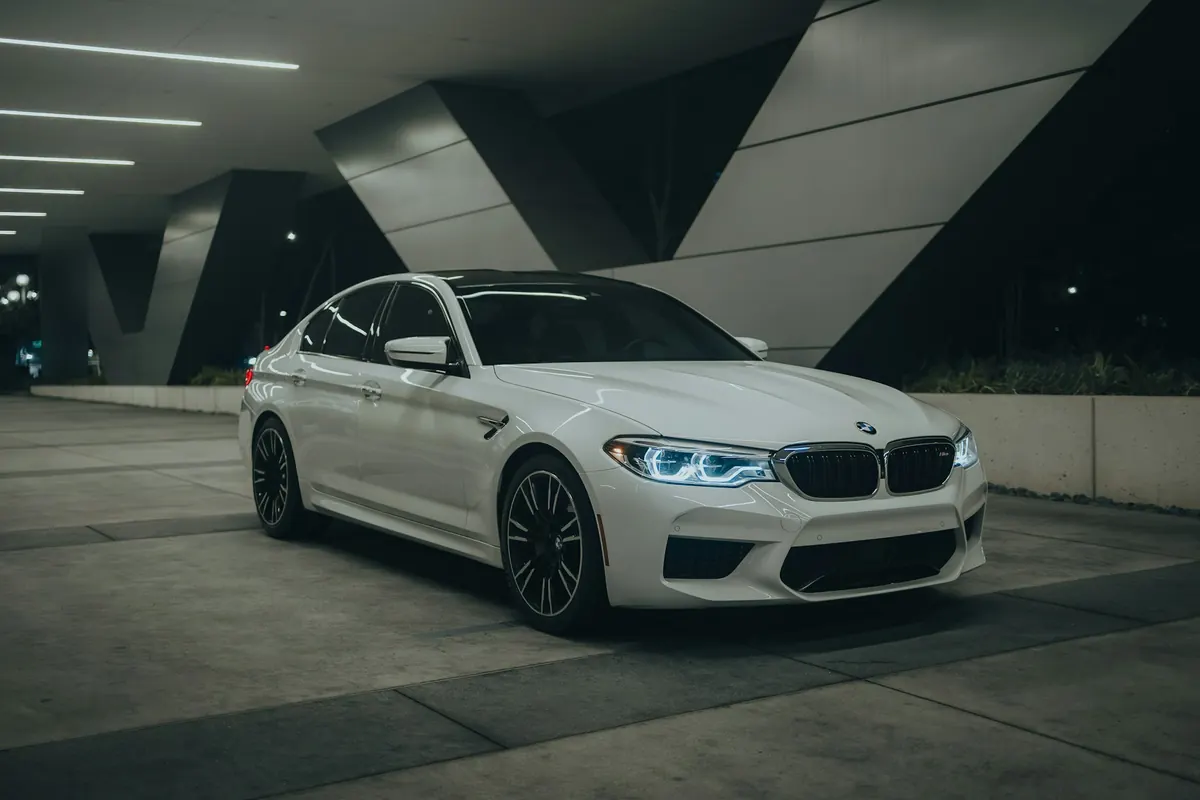 Front three-quarter view of a white BMW M5 (F90) parked under a modern building at night