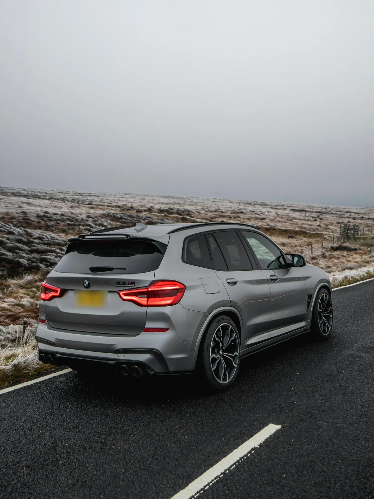 Rear three-quarter view of a grey BMW X3 M Competition (F97) on a moorland road