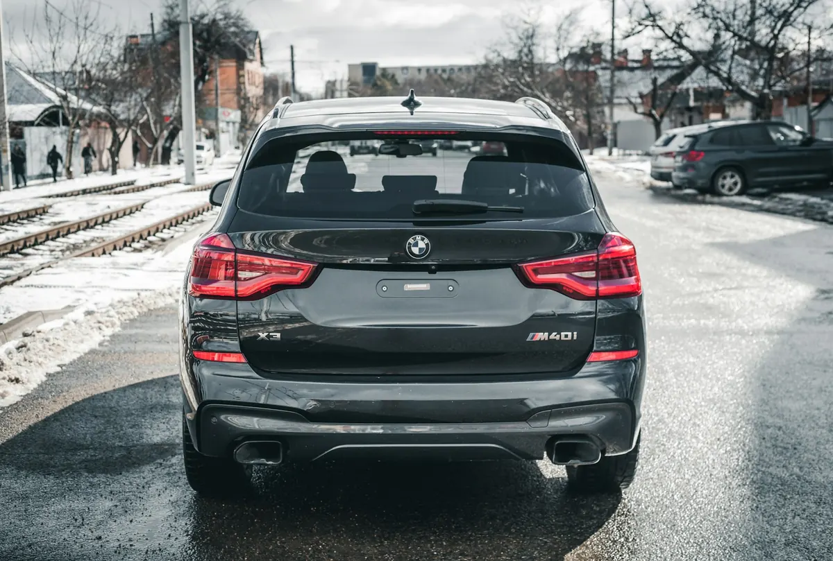 Rear view of a dark grey BMW X3 M40i (G01) on a wet winter street