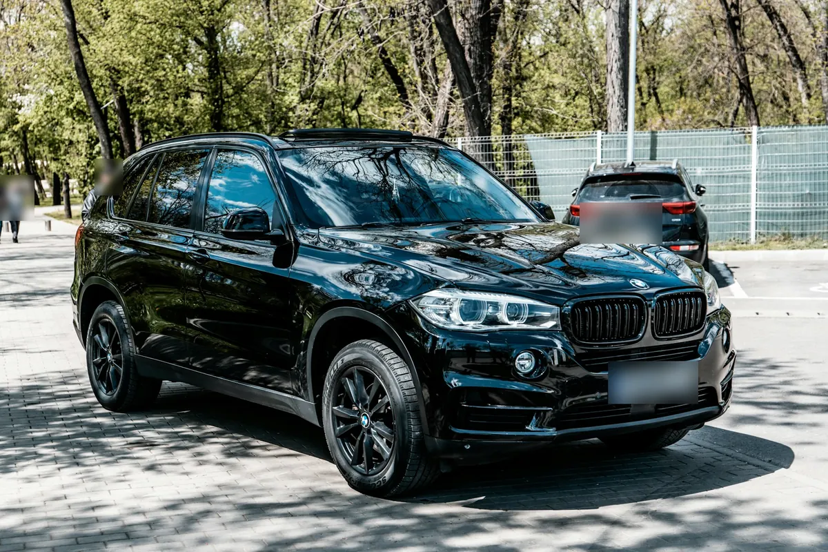 Front three-quarter view of a black BMW X5 xDrive50i (F15) in a tree-lined parking lot