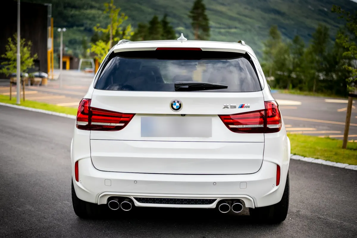 Rear view of a white BMW X5 M (F85) on a road below a green mountainside