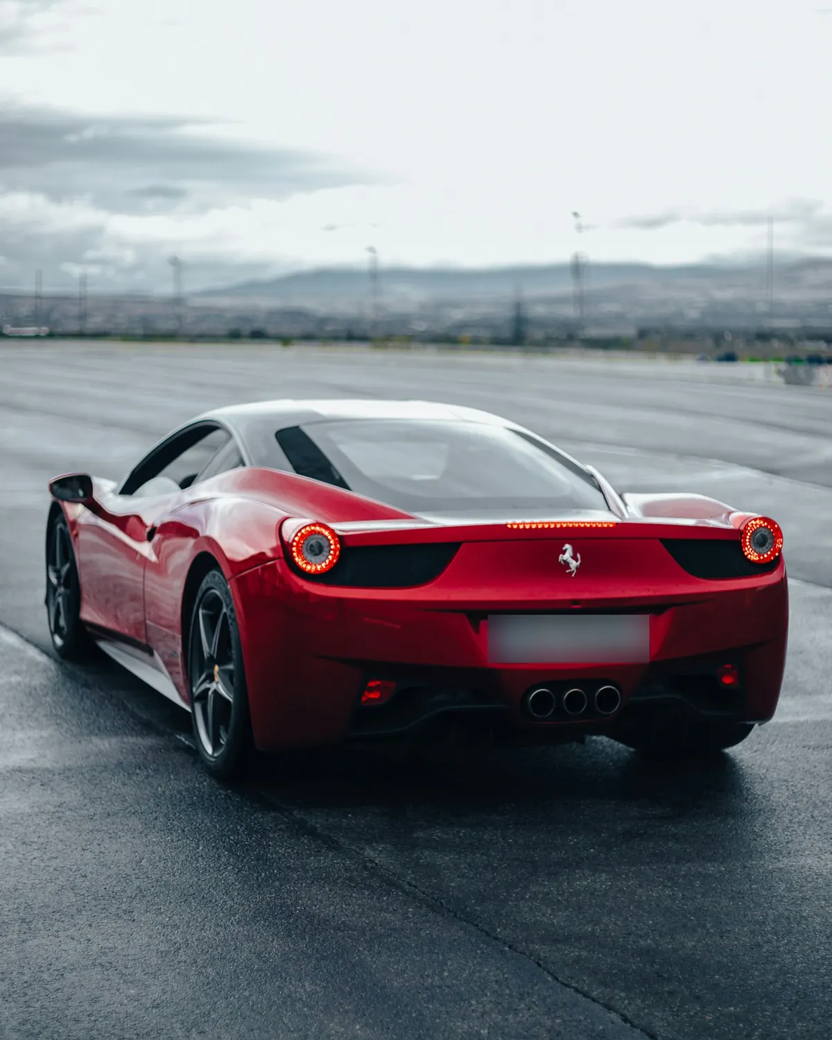 Rear three-quarter view of a red Ferrari 458 Italia on a wet test track