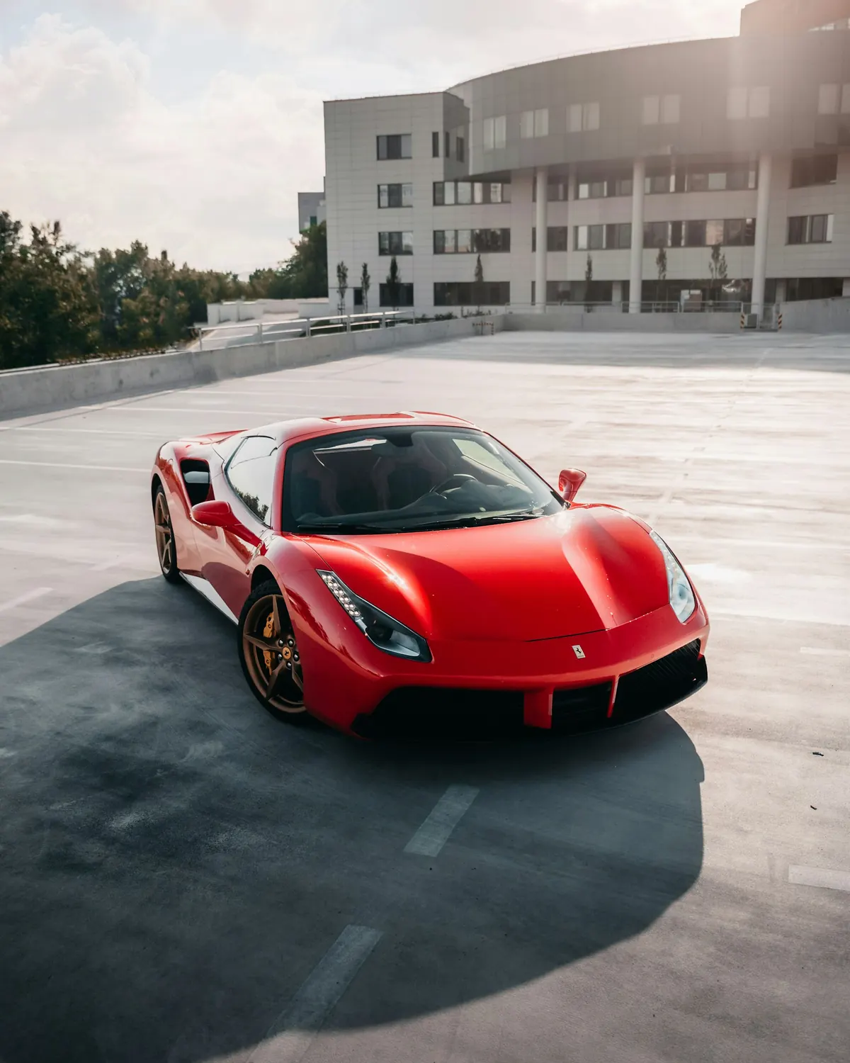 Front three-quarter view of a red Ferrari 488 GTB with gold wheels on a rooftop parking lot