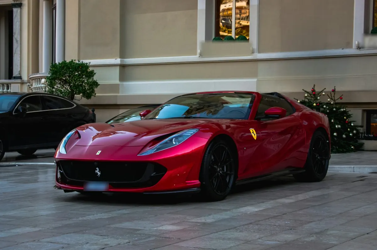 Front three-quarter view of a red Ferrari 812 GTS with the roof down, parked outside a building