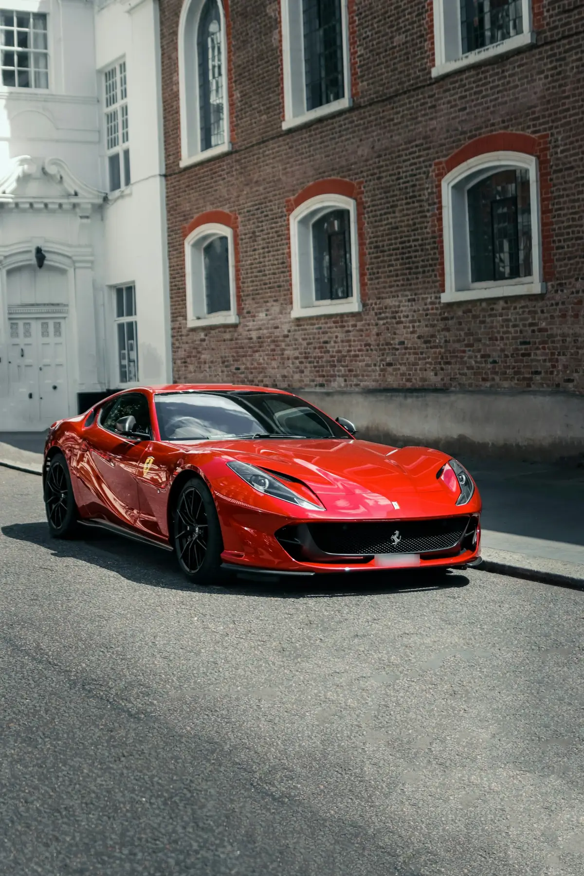 Front three-quarter view of a red Ferrari 812 Superfast parked in front of a brick building