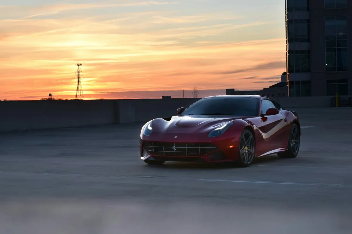 Front three-quarter view of a dark red Ferrari F12berlinetta on a rooftop parking lot at sunset
