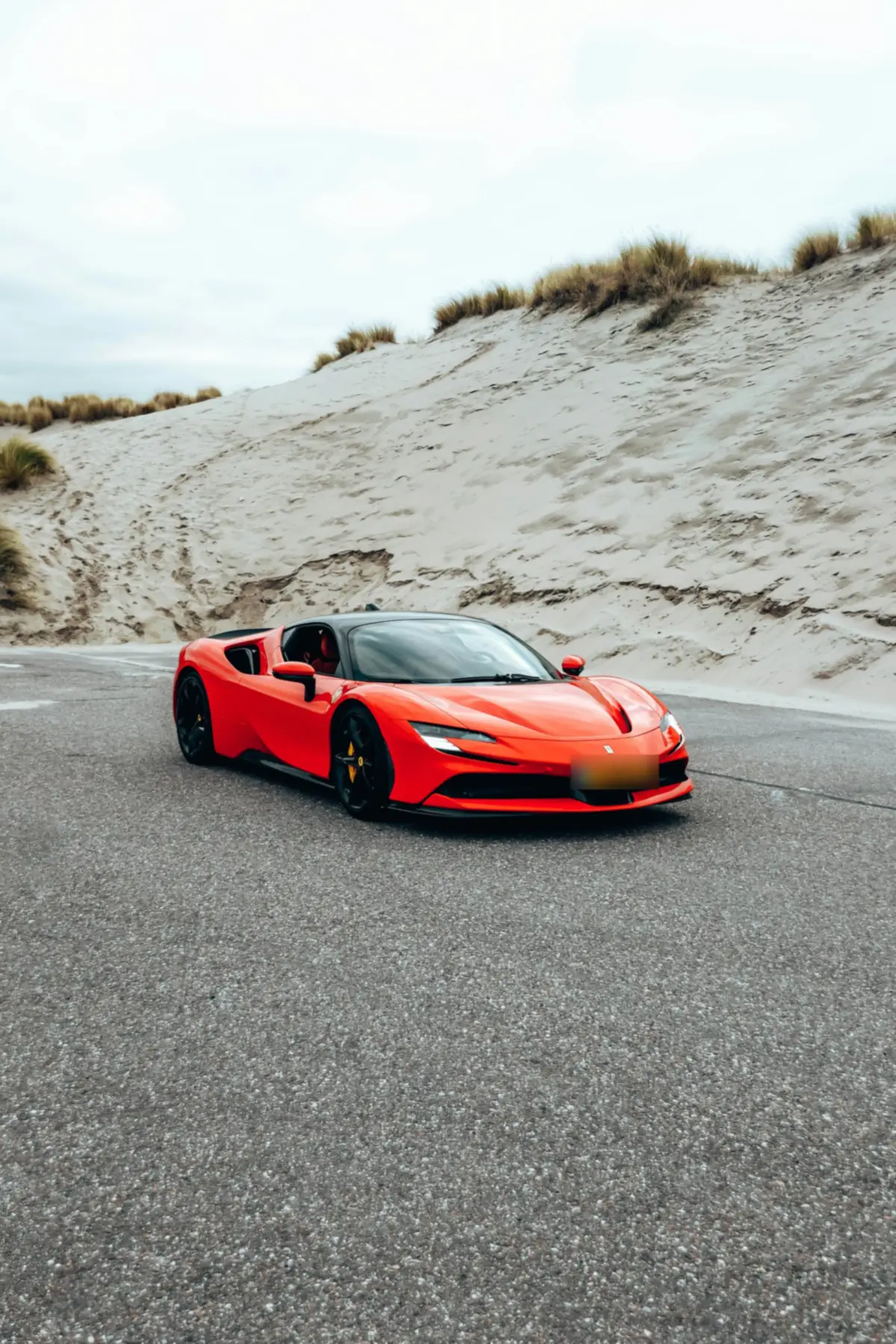 Front three-quarter view of a red Ferrari SF90 Stradale on a road between sand dunes