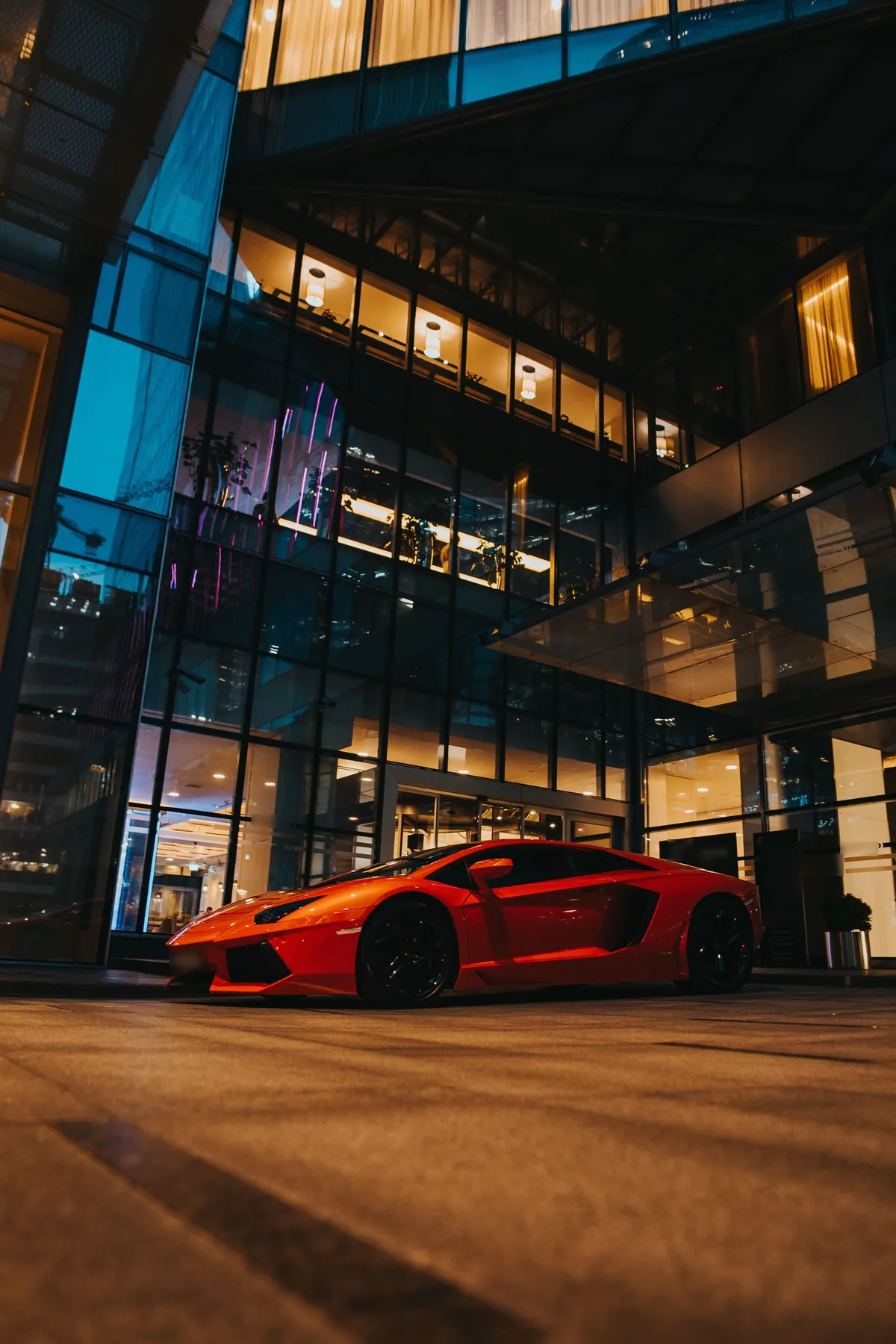 Front three-quarter view of a red Lamborghini Aventador LP 700-4 parked outside a glass building at night