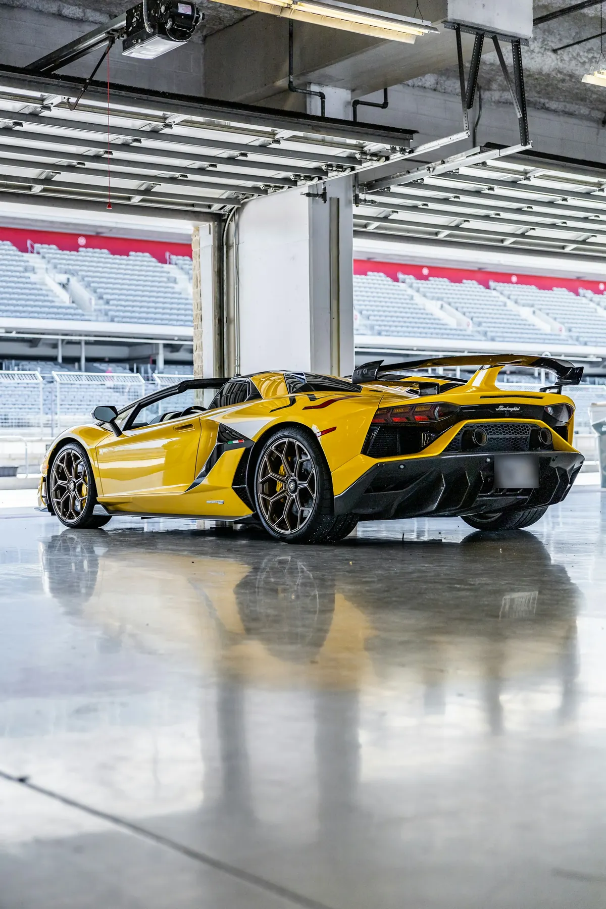 Rear three-quarter view of a yellow Lamborghini Aventador SVJ with the roof off in a pit garage