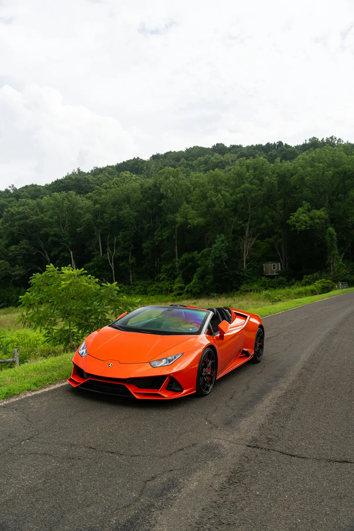 Front three-quarter view of an orange Lamborghini Huracán EVO with the roof down on a country road