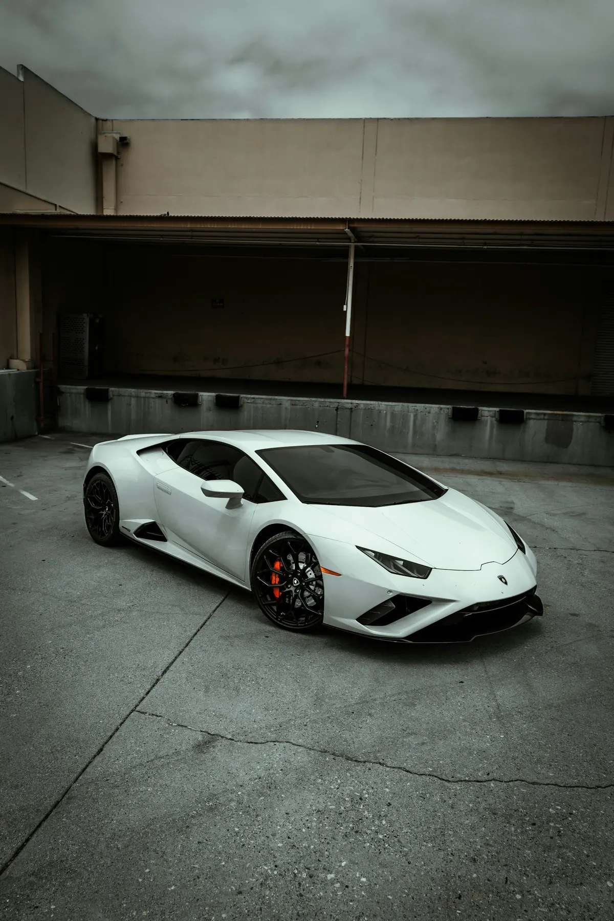 Front three-quarter view of a white Lamborghini Huracán EVO RWD coupe in a concrete loading yard